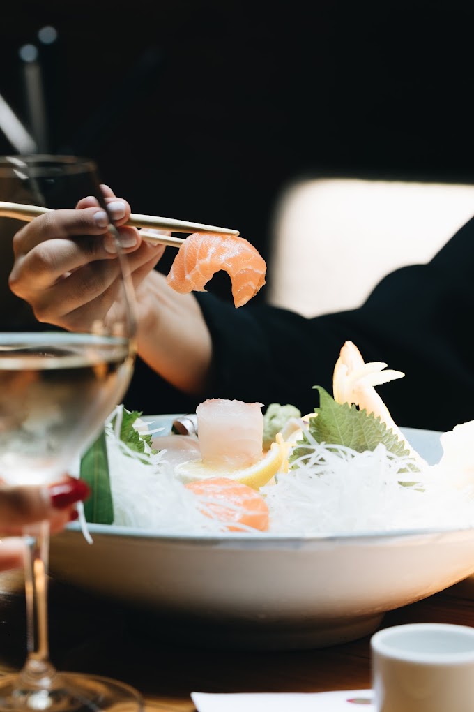 Persona comiendo laminas de salmon con arroz y una copa de vino