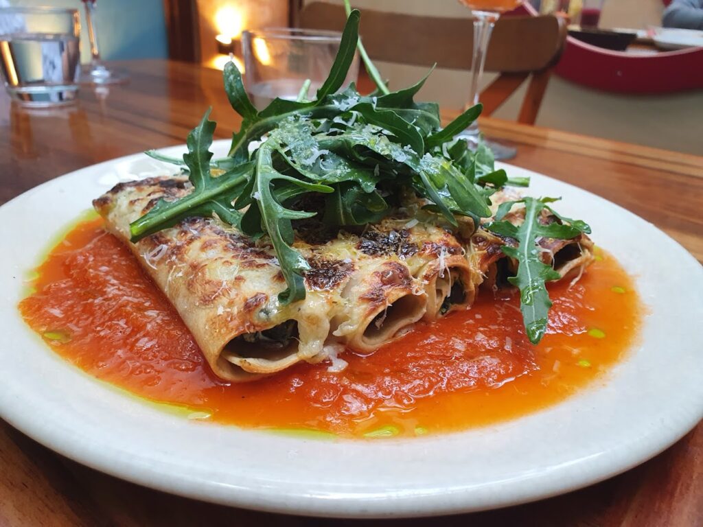 Torillas rellenas de carne, bañadas en salsa de tomate y como decoración unas hojas verdes